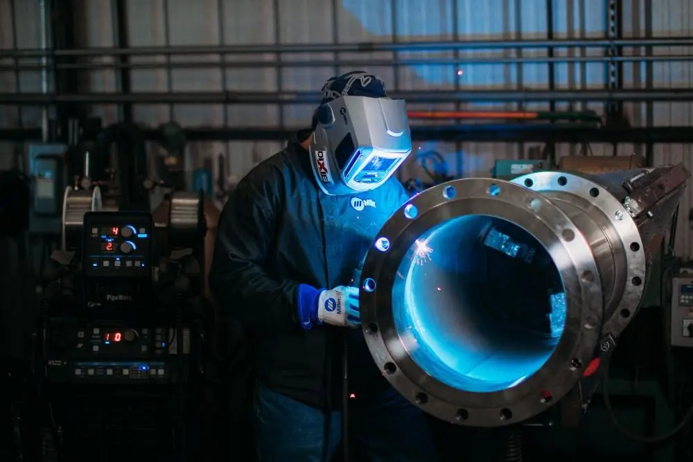 Welder performing pipe welding on large diameter steel pipe with blue arc light in industrial shop